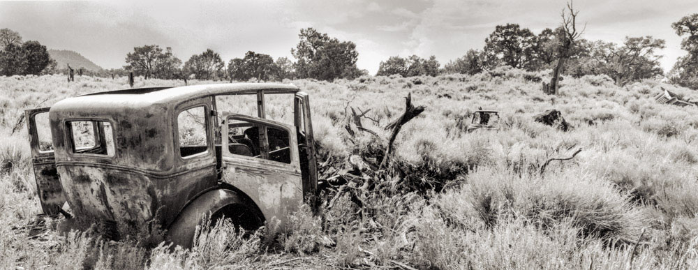 Pietown Car Abandoned vintage car rusting in a dry, overgrown field with trees in the background.