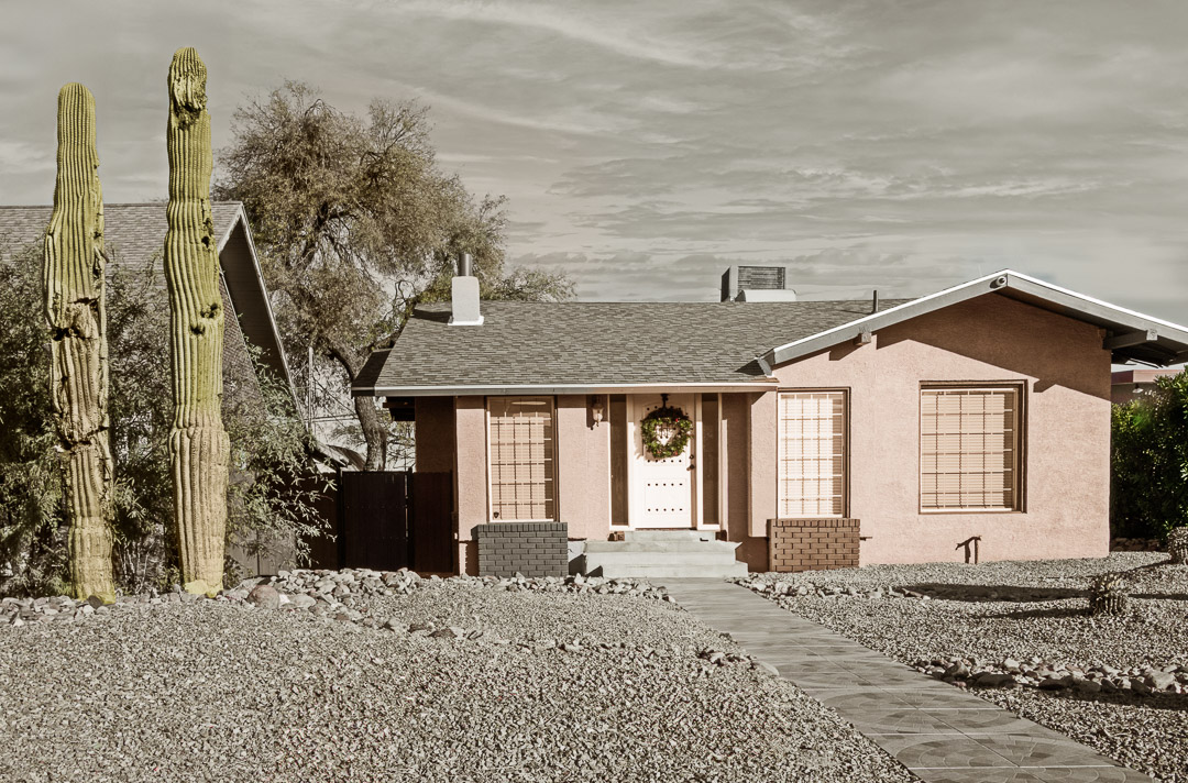 Small pink house with two giant cactus on left side of yard.