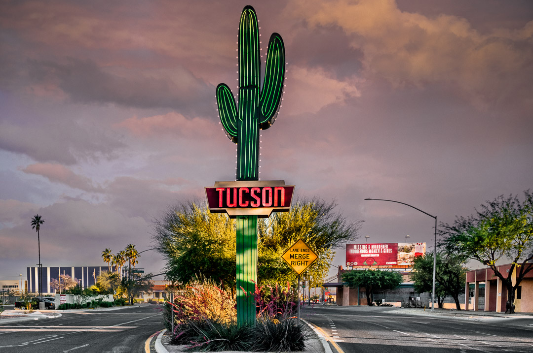 Neon saguaro in middle of large road in Tuscon with storm clouds in background.
